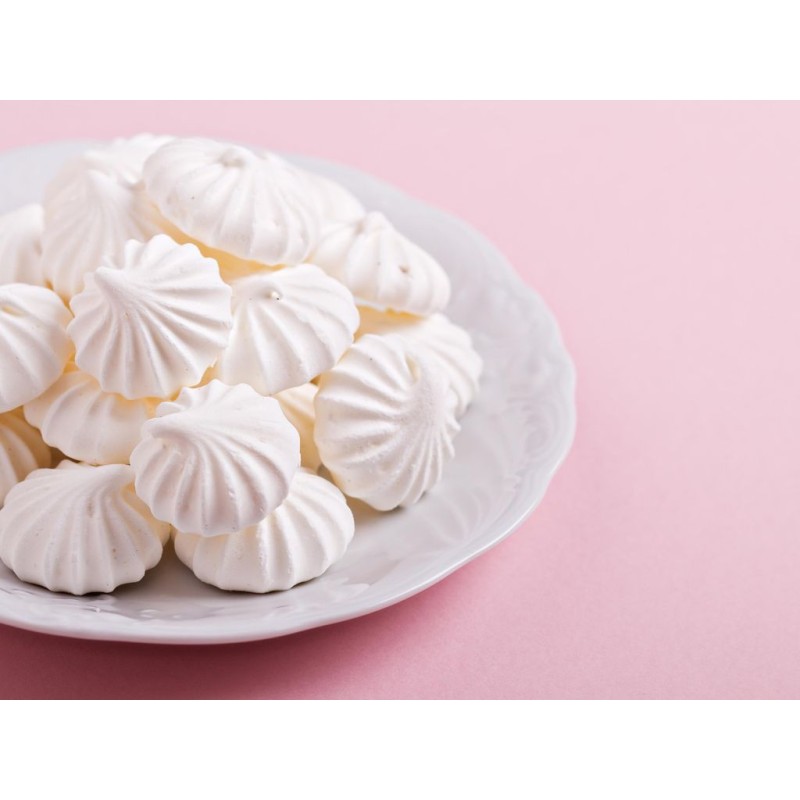 Petites meringues natures dans une assiette sur un fond rose